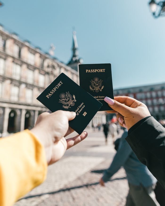 Crop unrecognizable travelers in casual clothes demonstrating passports of United States of America standing on square in historical city district